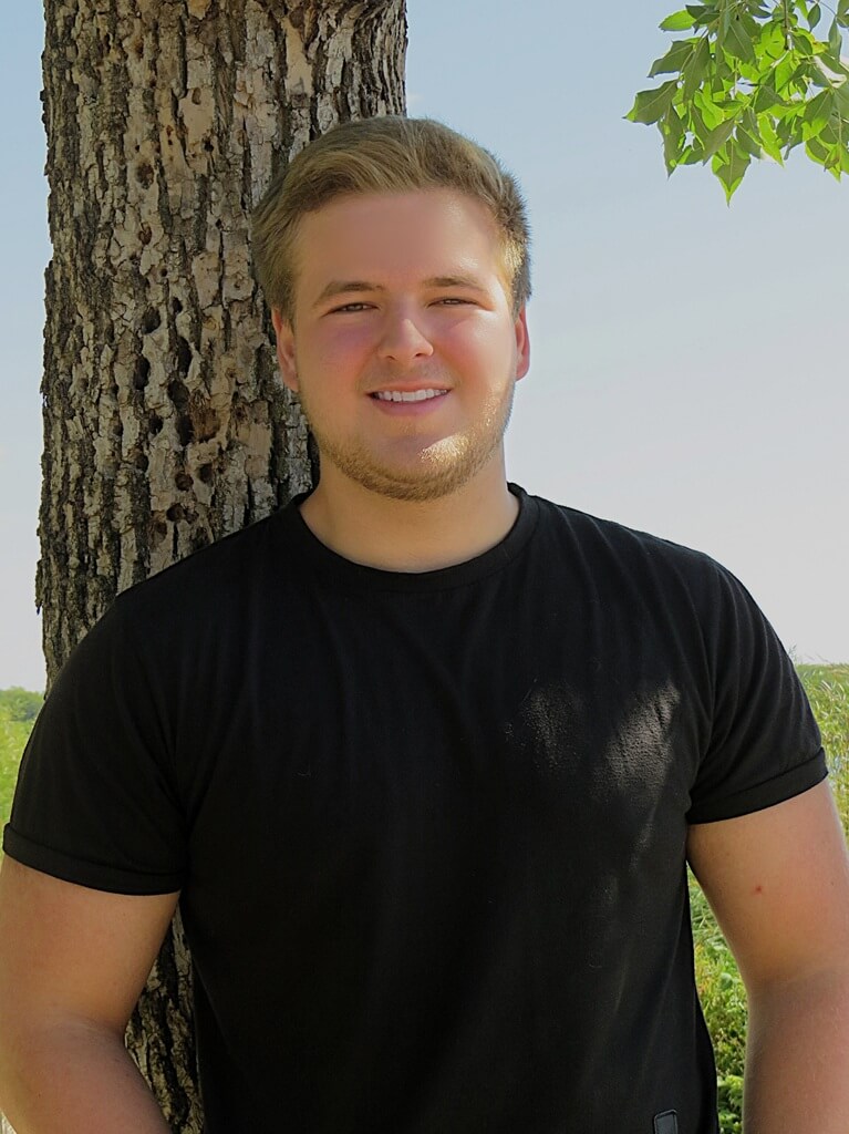Senior Photo of boy in black shirt by a large tree next to a field Senior photo of boy in black shirt and big smile by a tree by the field in the shade